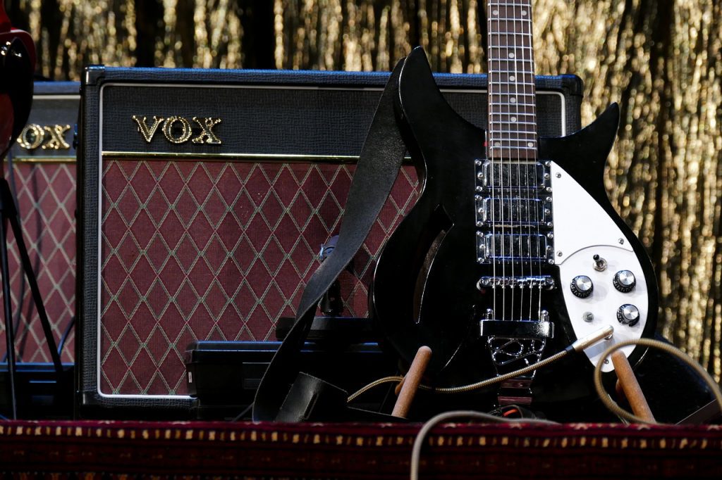 amplificador de guitarra preto da marca vox ao lado de uma guitarra preta e branca em pé